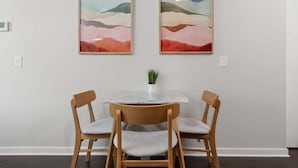 Comedor con una mesa de mármol y dos sillas de madera, con dos cuadros abstractos a cada lado.