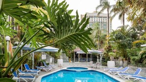 A pool area with lounge chairs and umbrellas, surrounded by tropical plants. - Unit 24-24 Hamilton Ave Surfers Paradise (Surfers Paradise)