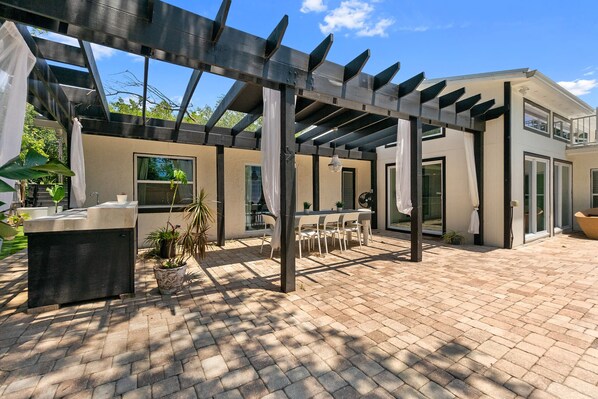 An outdoor patio with a pergola, a dining area, and a modern building with large windows.