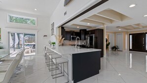 Una cocina moderna con una isla grande, taburetes de bar y un comedor con mesa de vidrio.