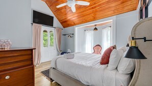 A bedroom with a wooden ceiling, a bed with white bedding, a dresser, and a nightstand with a lamp. - Urban Loft  l City Center l Walk to Everything! (St. Augustine)