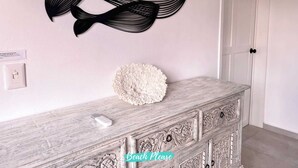 Une pièce avec une porte blanche, un mur blanc, un objet texturé blanc posé sur une commode en bois, et une œuvre d’art abstraite noire accrochée au mur.