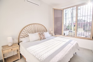 Un dormitorio con cama, mesita de noche, ventana y vistas al exterior.