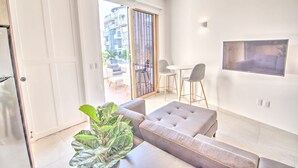 Un salon moderne avec un canapé, une petite table et un fauteuil. Une porte-fenêtre coulissante donne accès à un espace extérieur aménagé avec une table et des chaises.