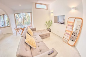 A modern living room with a sectional sofa, a TV mounted on the wall, and a balcony with large windows.