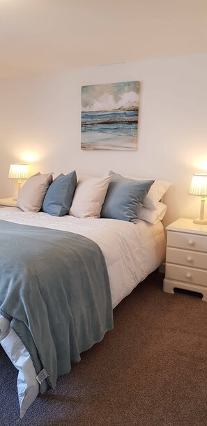A neatly made bed with a grey blanket and pillows, a painting of a beach scene on the wall, and two bedside lamps on white nightstands. - The Old Post Office. A cosy rural gem -  Dartmoor (Ponsworthy)