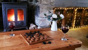 Ein Holztisch mit Schachbrett, zwei Gläser Rotwein, einer Blumenvase und einem Kamin im Hintergrund.