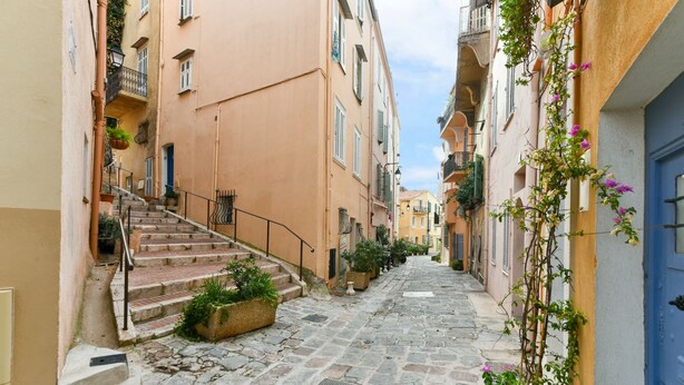 Une ruelle étroite pavée, bordée d’immeubles dotés de balcons et de plantes en pot.