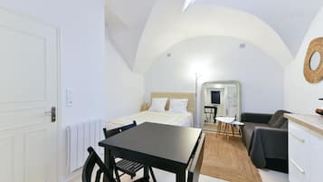 Et kompakt, godt oplyst værelse med seng, lille spisebord med stole, sofa og tekøkken.