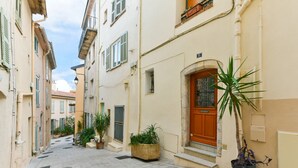 Une rue étroite, bordée de bâtiments des deux côtés, avec une porte en bois et des plantes en pot.