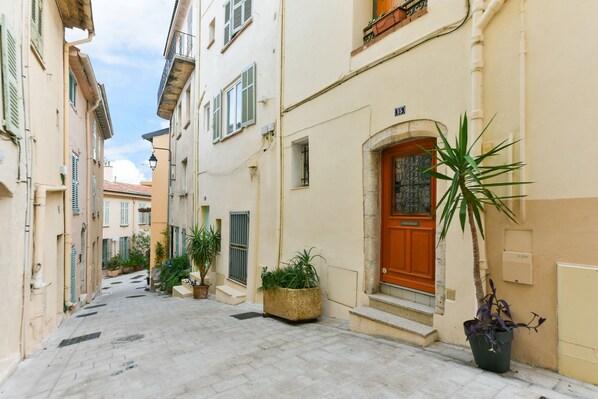 A narrow street with buildings on either side, featuring a wooden door and potted plants.
