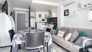 A modern, compact living space with a dining area, kitchenette, and a sofa with cushions. - Le Royal Studio adorable avec terrasse (Cannes)