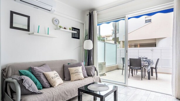 A modern living room with a sofa, a small table, and a balcony with a dining area. - Le Royal Studio adorable avec terrasse (Cannes)