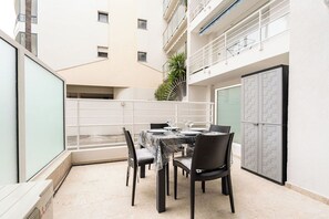 A dining area with a table set for four, surrounded by chairs, in a building with a balcony and a view of the surrounding area. - Le Royal Studio adorable avec terrasse (Cannes)