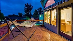 A wooden deck with a hammock, a glass-enclosed room with a sofa, and a view of trees. - Backyard Oasis Pool | Beautiful Home (Arvada)