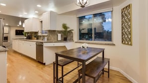 A modern kitchen with white cabinets, a wooden dining table, and a large window with a view. - Backyard Oasis Pool | Beautiful Home (Arvada)