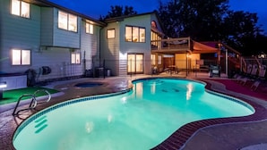 A swimming pool with a curved edge, surrounded by a fence, and a building with multiple windows and a balcony. - Backyard Oasis Pool | Beautiful Home (Arvada)