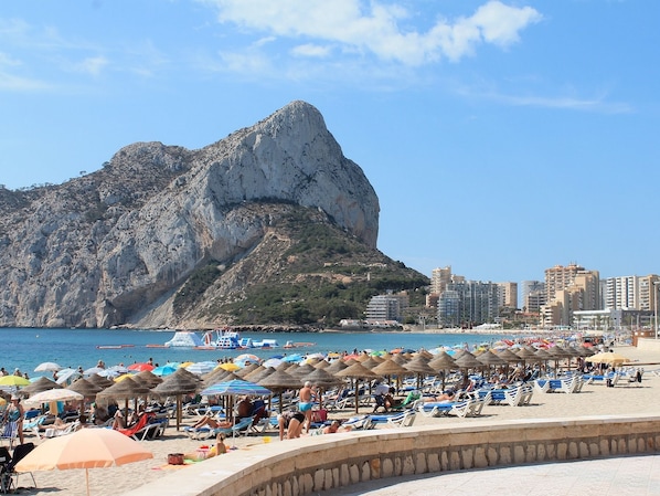 A beach with sun loungers and umbrellas, a rocky mountain in the background, and a cityscape with buildings. - Alexia I 92 - Grupo Turis - Calpe, Costa Blanca (Calpe)