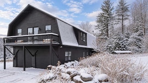 Casa de dos pisos con un balcón, rodeada de un paisaje y árboles cubiertos de nieve.