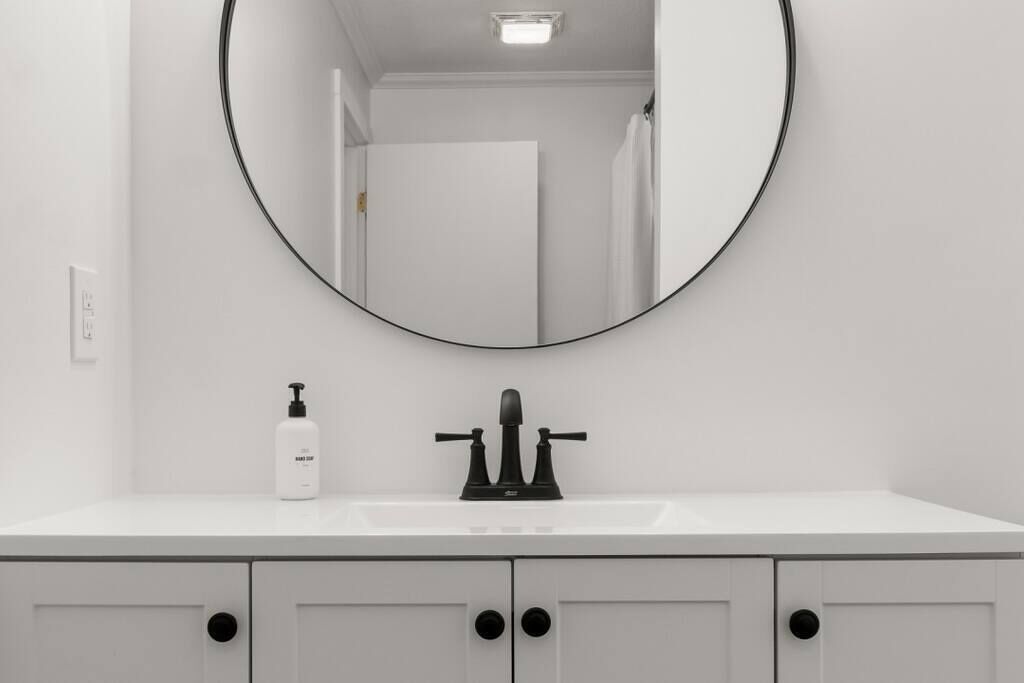 A bathroom with a round mirror, a white sink, and a bottle of hand soap.