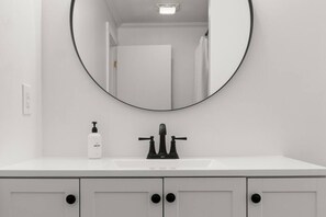 A bathroom with a round mirror, a white sink, and a bottle of hand soap. - Hilltop 5-BR Carriage House 4-Min to Okemo (Ludlow)