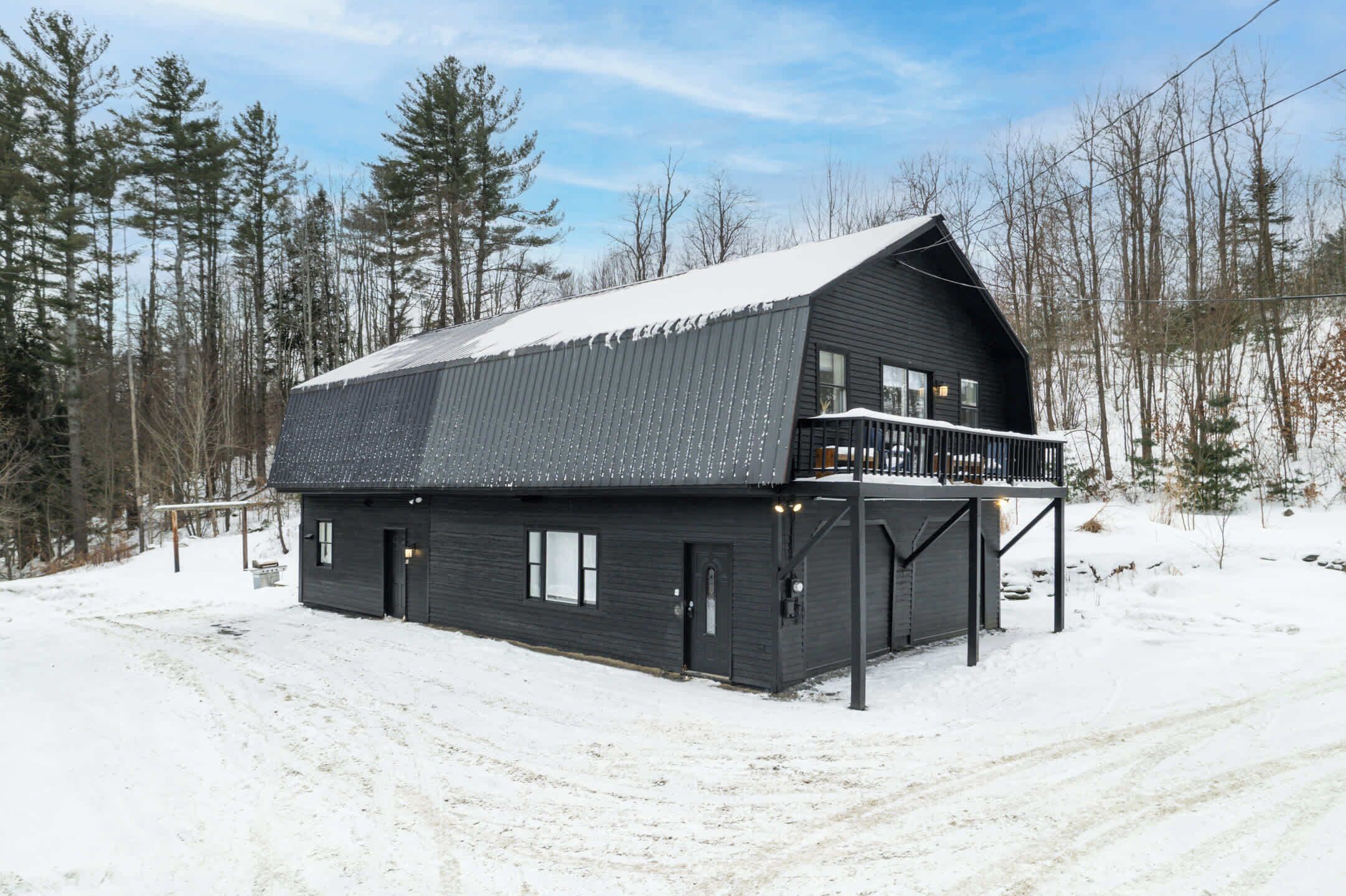 Una cabaña de madera oscura con un balcón, rodeada de nieve y árboles.