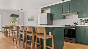 Una cocina moderna con gabinetes verdes, una isla central con taburetes de bar, una estufa y un refrigerador.