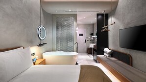 Une chambre d’hôtel moderne avec un grand lit, une baignoire, un miroir, une télévision et un mur en briques.