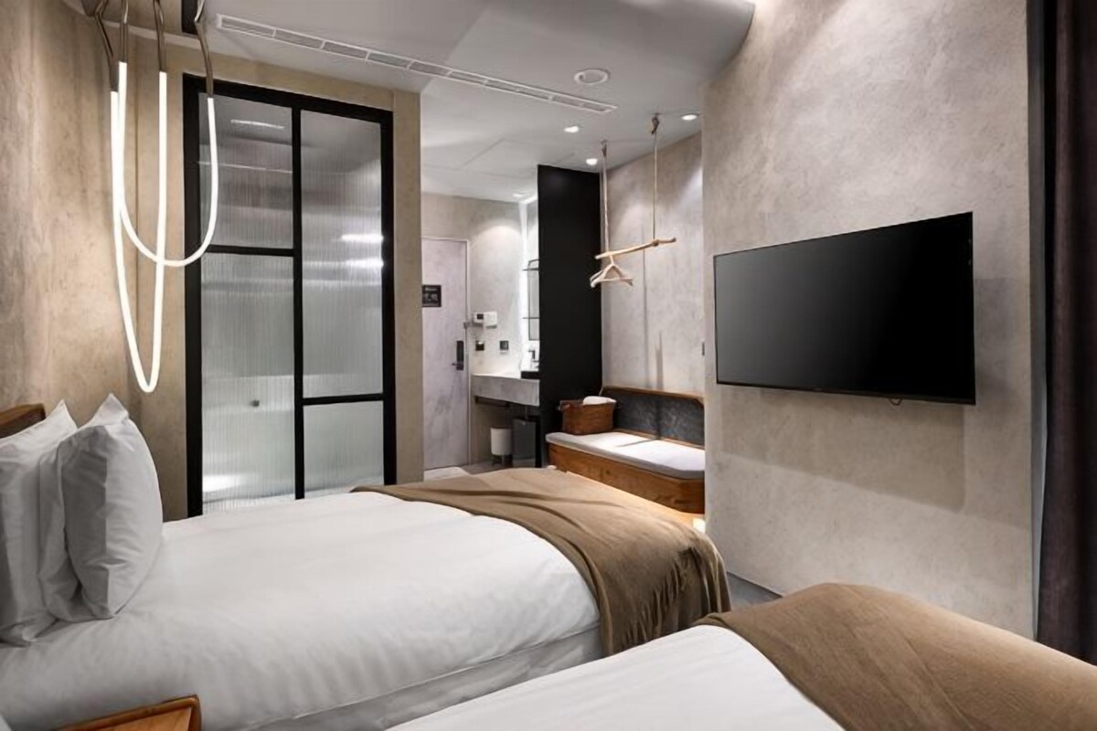 Ein modernes Hotelzimmer mit zwei Betten, einem Flachbildfernseher, einem großen Spiegel und einem Schiebetürenschrank.