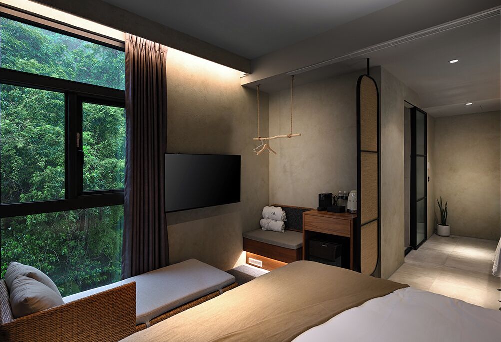 A modern hotel room with a large window, a bed, a bedside table, a TV, and a wardrobe.