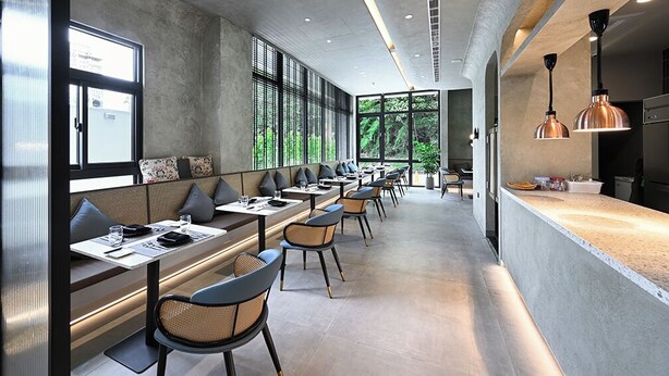 Un restaurant moderne avec de longues tables et des banquettes, de grandes fenêtres et un espace cuisine.