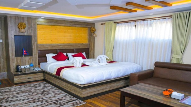 A hotel room with a wooden headboard, a large bed with white bedding and red pillows, a brown sofa, a wooden coffee table, and a blue rug.