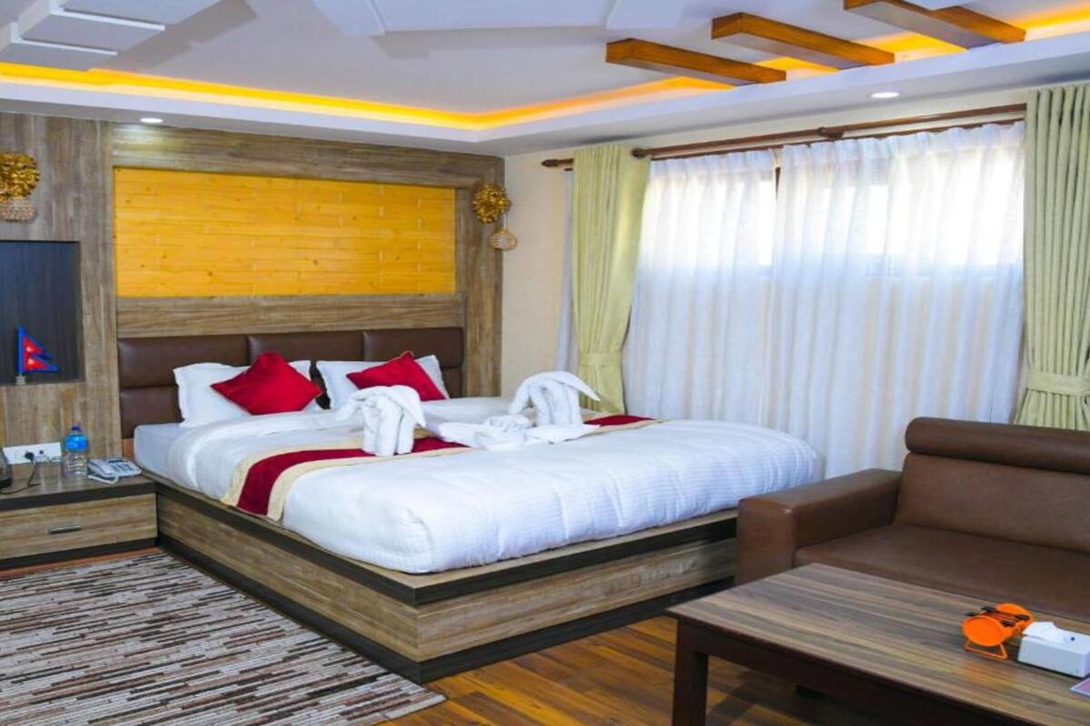 A hotel room with a wooden headboard, a large bed with white bedding and red pillows, a brown sofa, a wooden coffee table, and a blue rug.