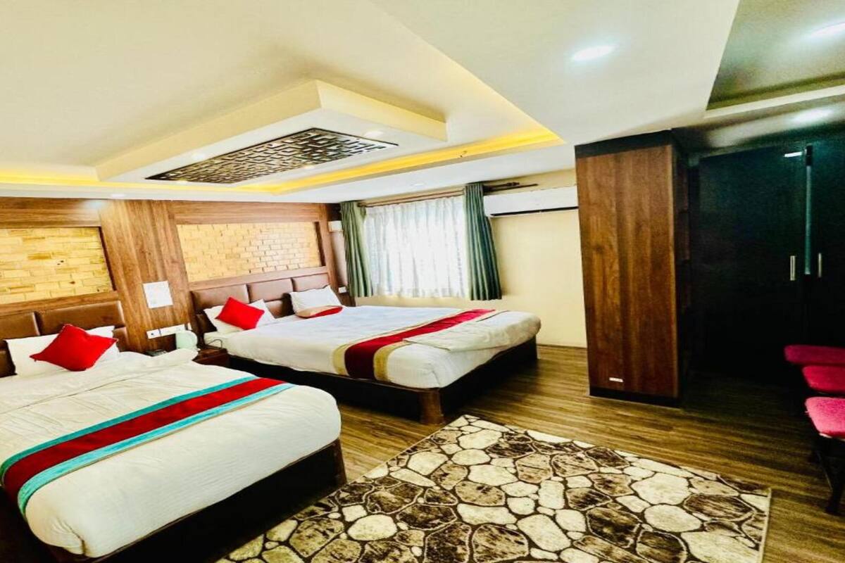 A hotel room with two beds, a stone-patterned rug, wooden walls, and a wardrobe.