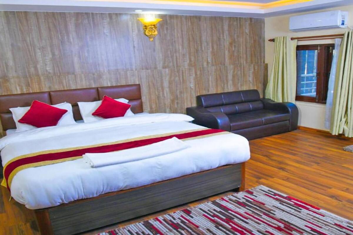 A bedroom with a large bed, a leather sofa, wooden flooring, and a window with curtains.