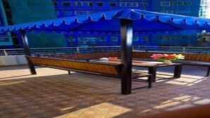 A covered seating area with benches and a table, featuring a view of buildings in the background.