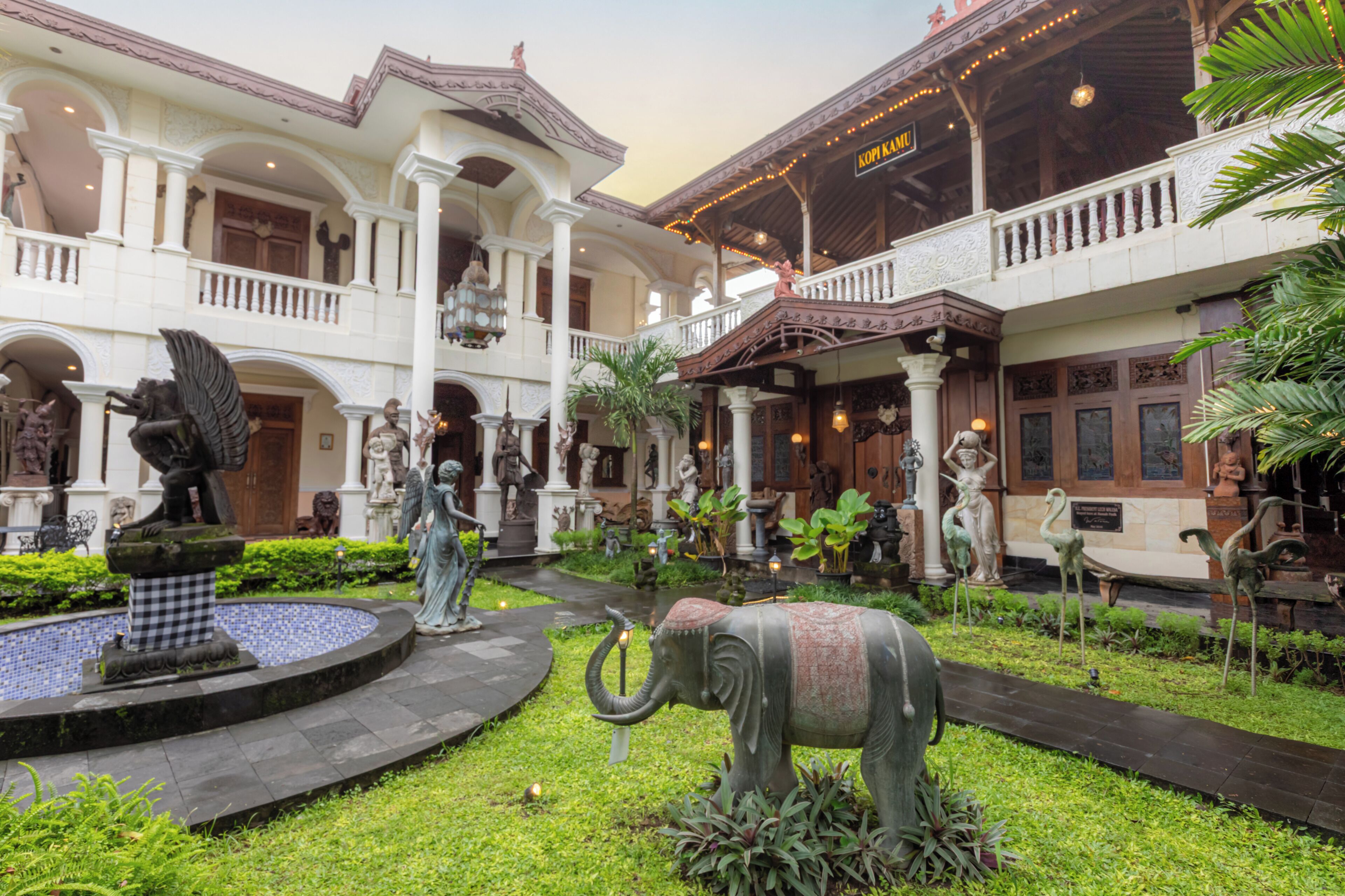 Une cour avec une fontaine, des statues et une grande statue d’éléphant.