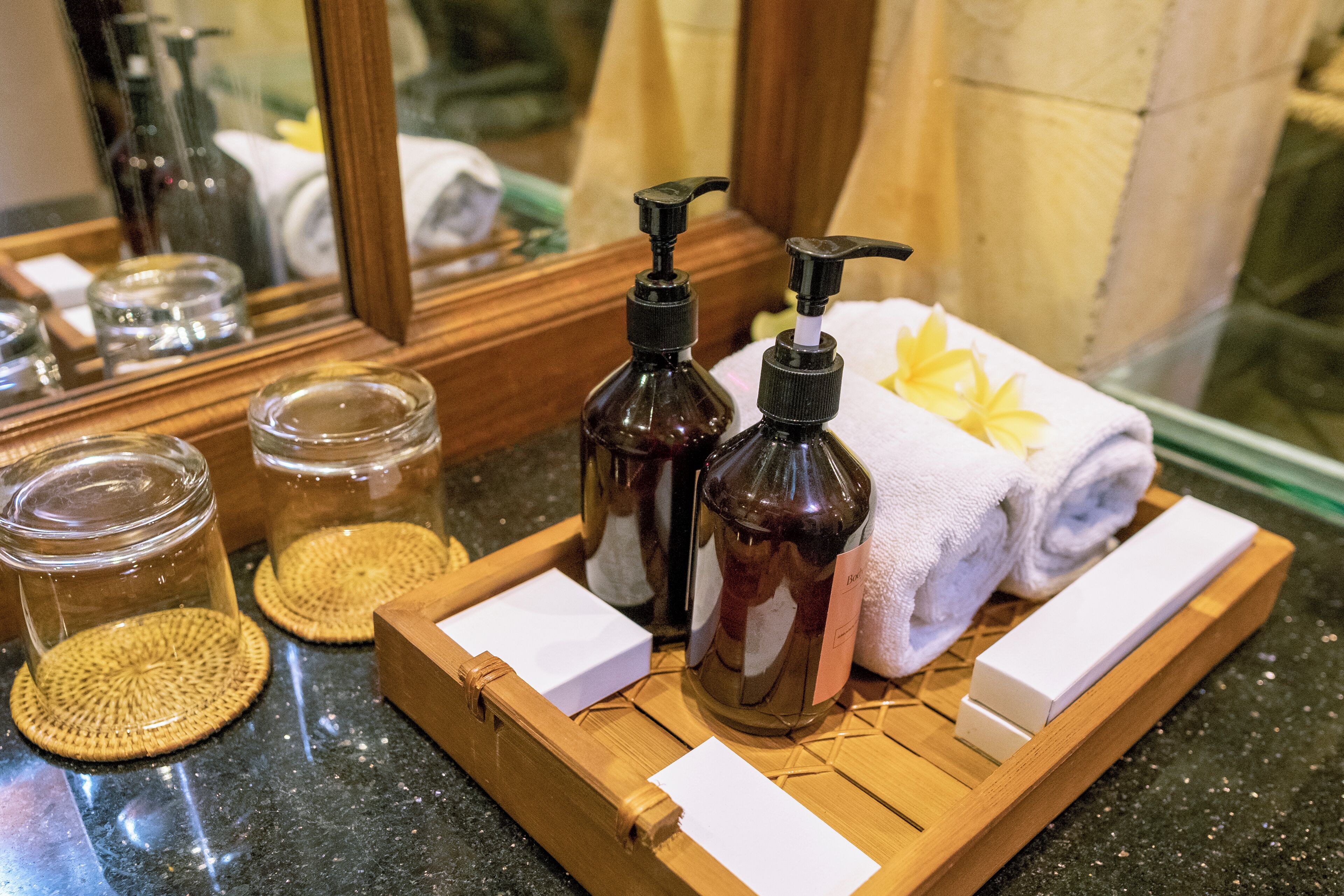 A wooden tray with toiletries, a towel, and a mirror reflecting a bathroom setting.