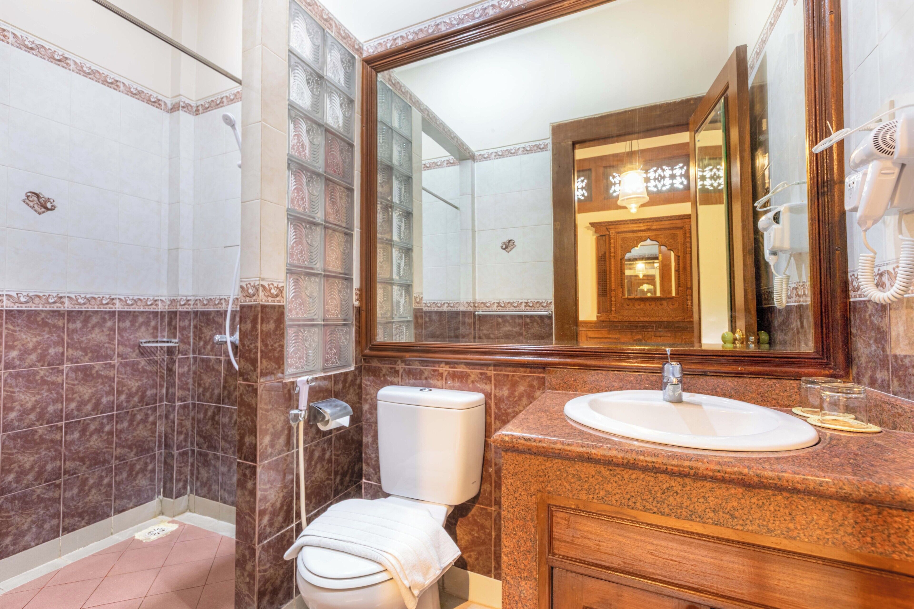 Un baño con inodoro, lavamanos, ducha y un espejo grande.