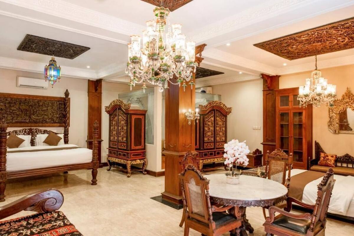 Una habitación con una cama, una mesa de comedor con sillas y dos armarios de madera decorados.
