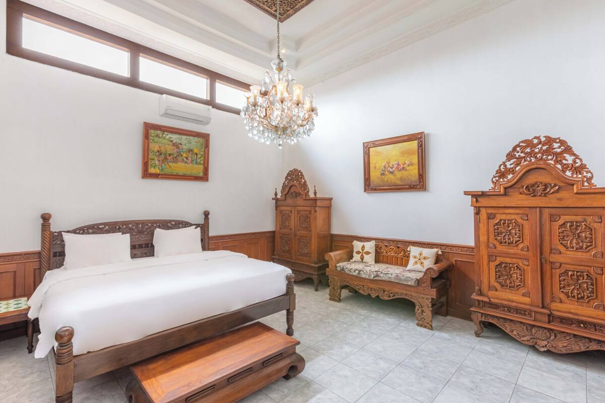 Un dormitorio con una cama de madera, un candelabro, un armario de madera y dos cuadros en la pared.