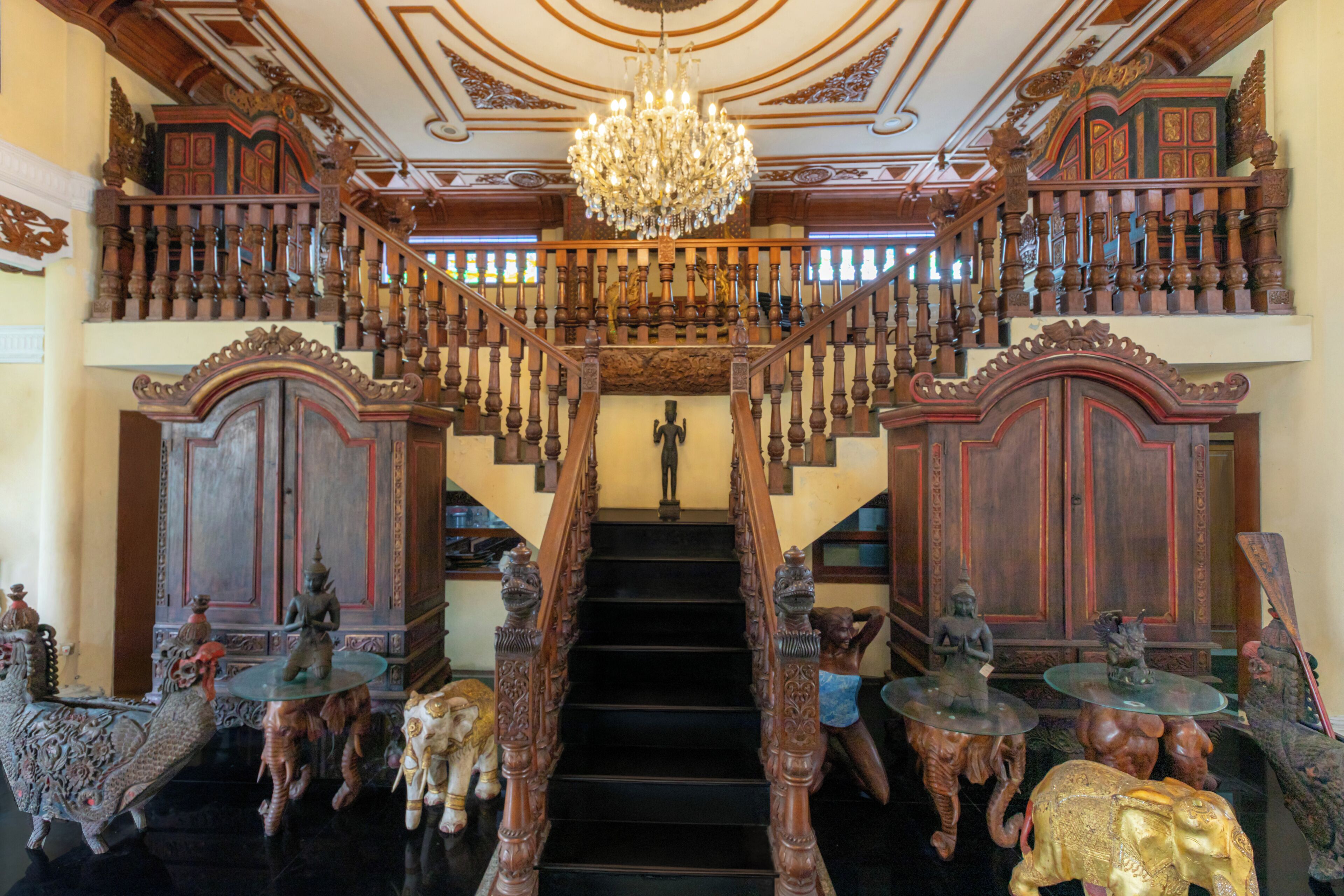A grand staircase with ornate railings and a chandelier, leading to a second-floor balcony with a view.