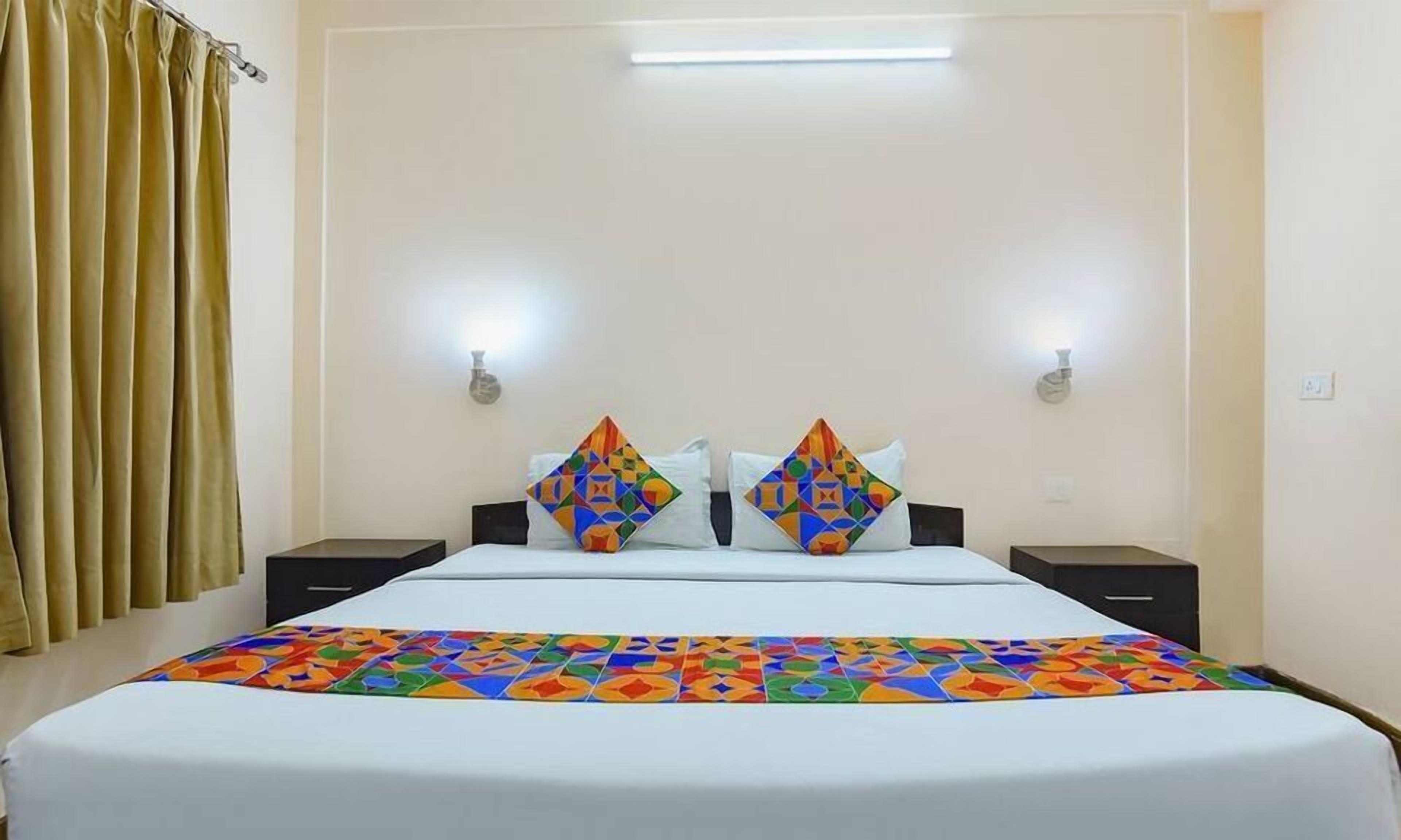 Una habitación de hotel con una cama, dos mesitas de noche, una colcha colorida y una cortina.