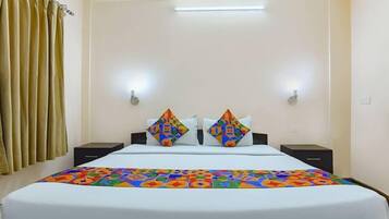 Una habitación de hotel con una cama, dos mesitas de noche, una colcha colorida y una cortina.