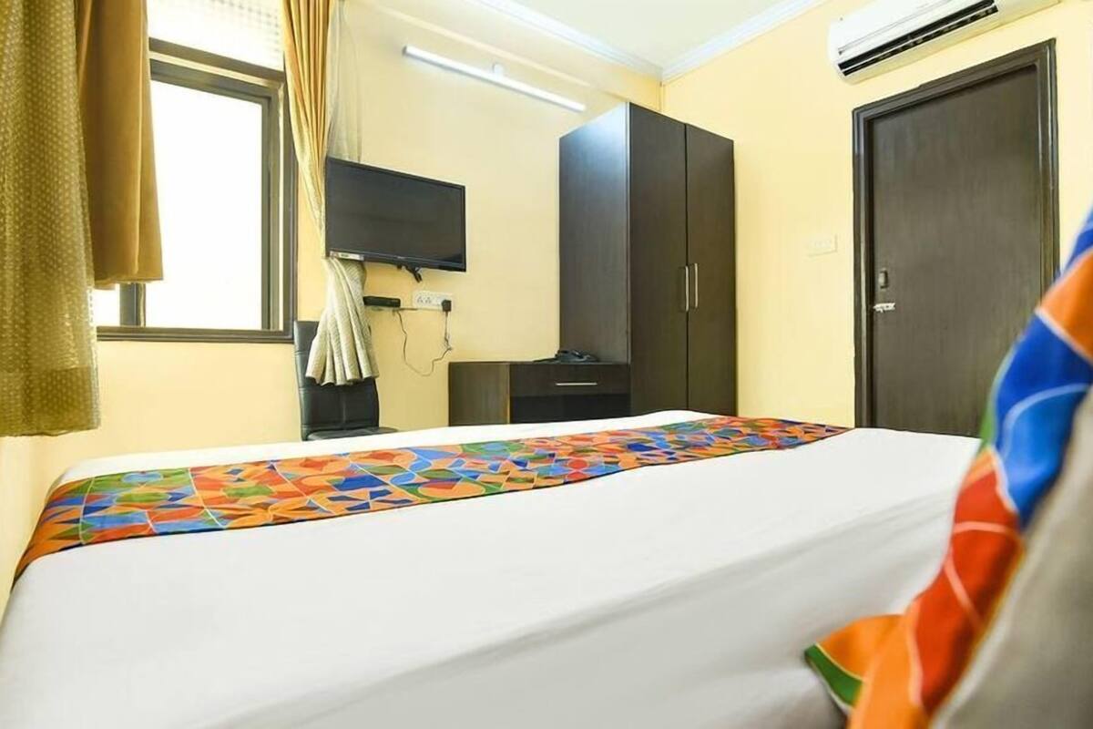 Quarto de hotel com cama, televisão, guarda-roupa e janela com cortinas.