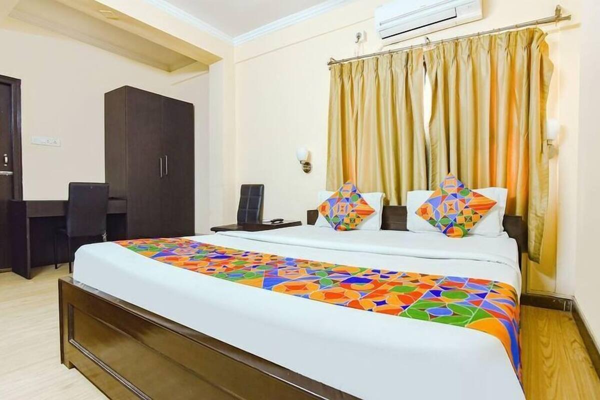 Quarto de hotel com cama, escrivaninha, guarda-roupa e cortina.