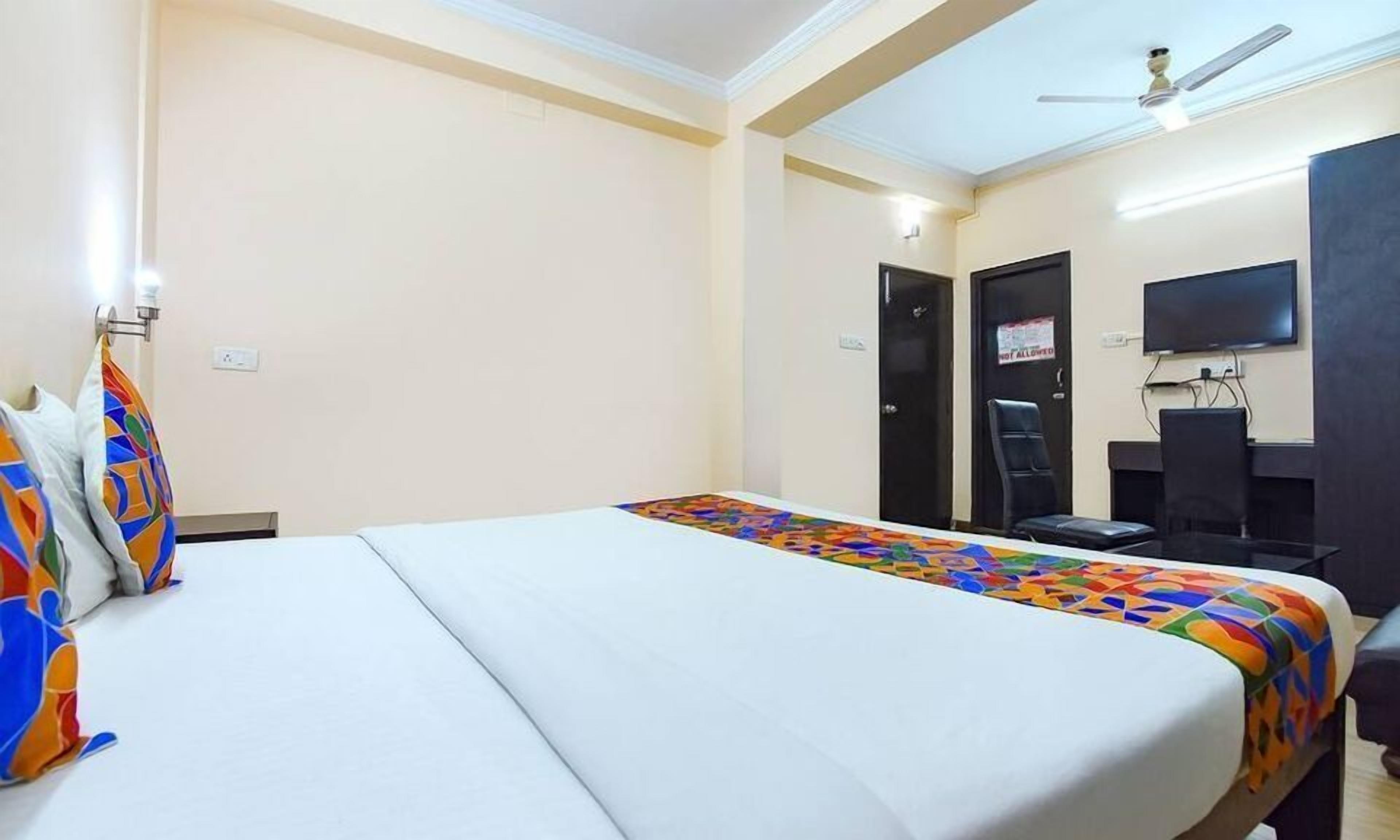 Una habitación de hotel con cama, escritorio, silla, televisor y ventilador de techo.