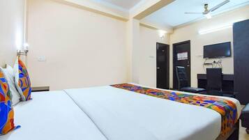 Una habitación de hotel con cama, escritorio, silla, televisor y ventilador de techo.