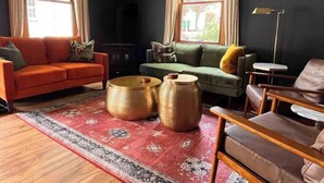 A modern living room with a red sofa, green sofa, and a brown leather chair. There are two round wooden tables and a large patterned rug. - Modern Victorian in the heart of downtown Nevada City (Nevada City)
