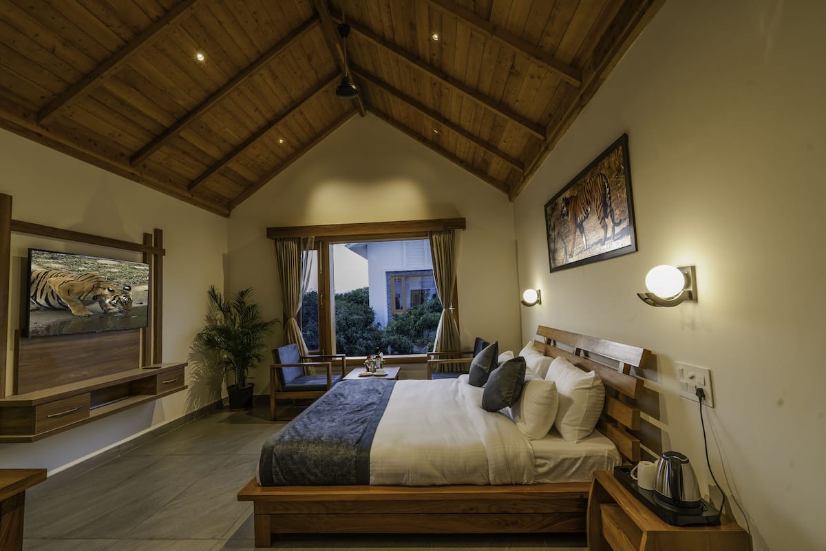 Un dormitorio con techo de madera, una cama con almohadas, una mesita de noche, un televisor y una ventana con cortinas.